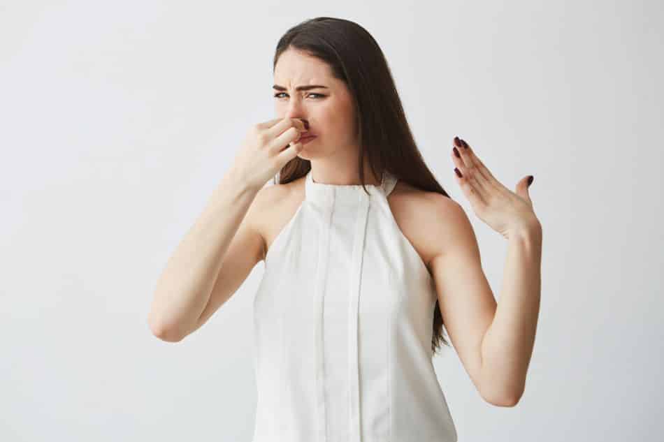 Young brunette girl closing covering nose over white background. Bad smell.